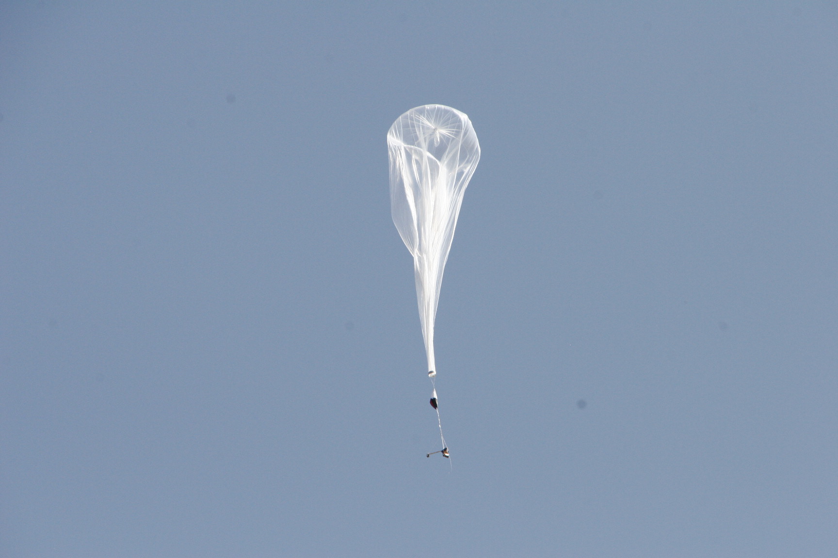 Thin-sheet balloon flies in blue sky with payload